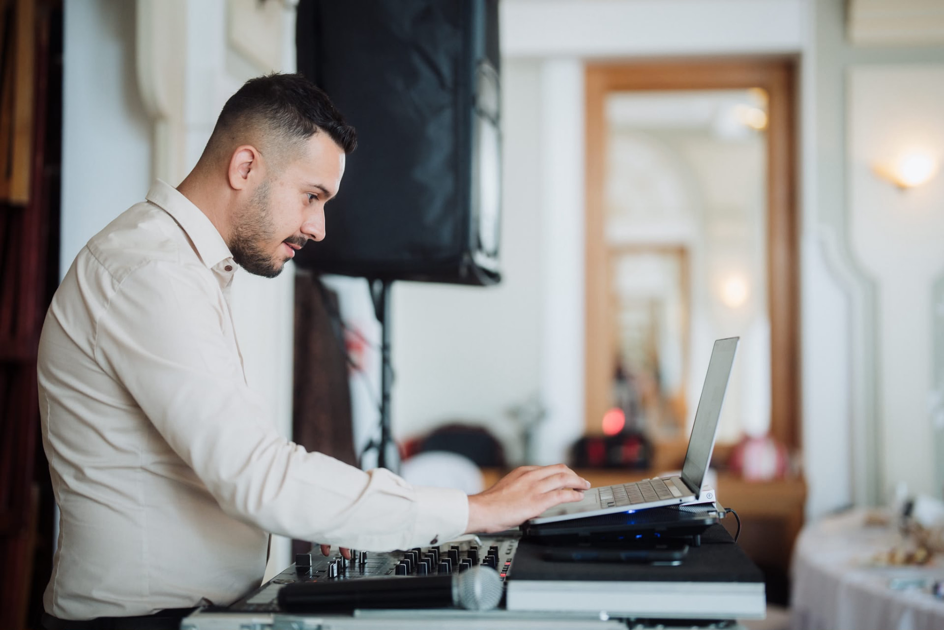 DJ la consolă, cu laptop, într-o sală luminoasă de eveniment